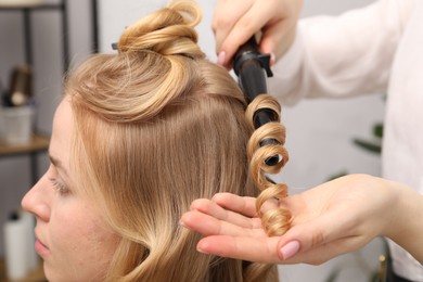 Photo of Hairdresser curling woman's hair in salon, closeup