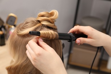 Photo of Hairdresser curling woman's hair in salon, closeup