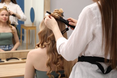 Photo of Hairdresser curling woman's hair in salon, closeup