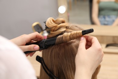 Photo of Hairdresser curling woman's hair in salon, closeup