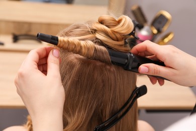 Photo of Hairdresser curling woman's hair in salon, closeup