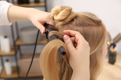 Photo of Hairdresser curling woman's hair in salon, closeup