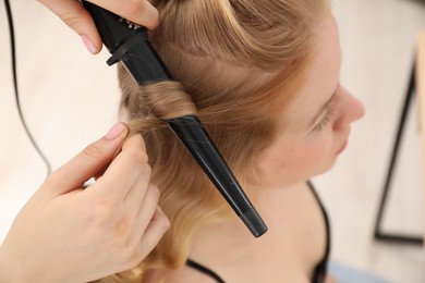 Photo of Hairdresser curling woman's hair in salon, closeup