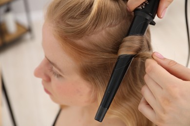 Photo of Hairdresser curling woman's hair in salon, closeup