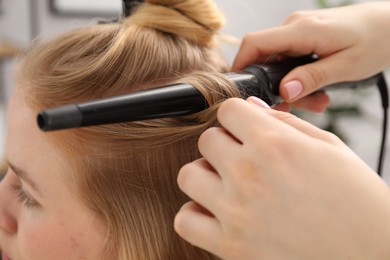 Photo of Hairdresser curling woman's hair in salon, closeup