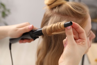 Photo of Hairdresser curling woman's hair in salon, closeup