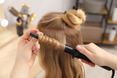 Photo of Hairdresser curling woman's hair in salon, closeup
