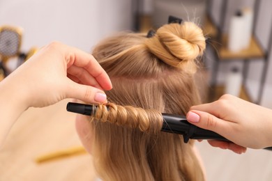 Photo of Hairdresser curling woman's hair in salon, closeup