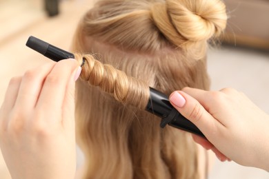 Photo of Hairdresser curling woman's hair in salon, closeup