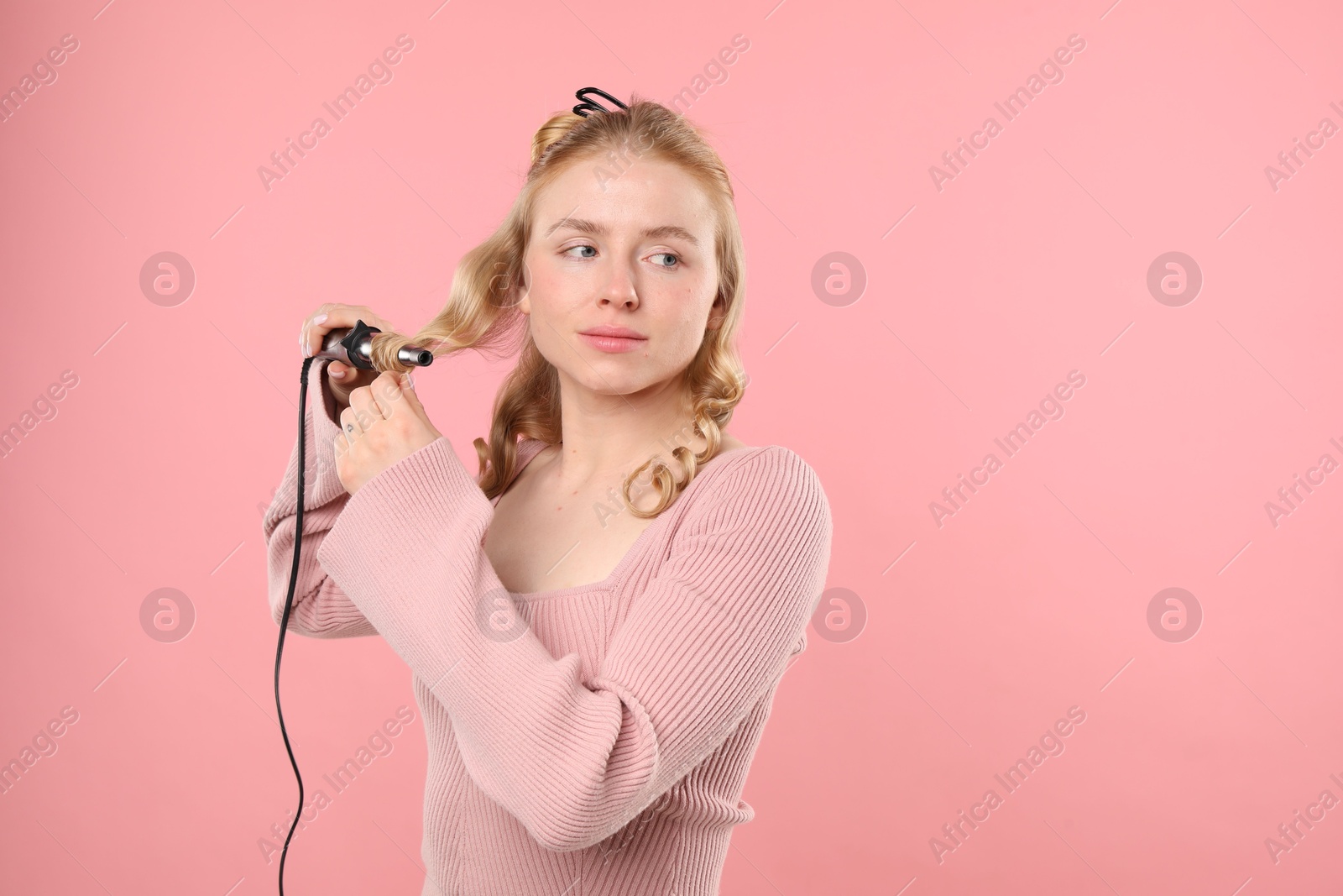 Woman curling her hair on pink background. Space for text Photo of Woman curling her hair on pink background. Space for text