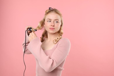 Photo of Woman curling her hair on pink background. Space for text