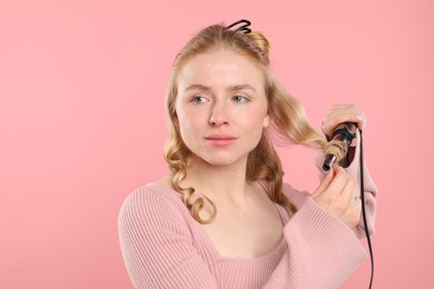 Photo of Woman curling her hair on pink background. Space for text
