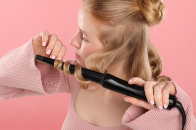 Photo of Woman curling her hair on pink background