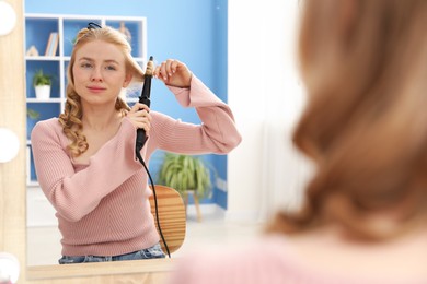 Photo of Woman curling her hair near mirror indoors