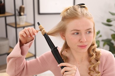 Photo of Woman styling her beautiful hair with curling iron indoors