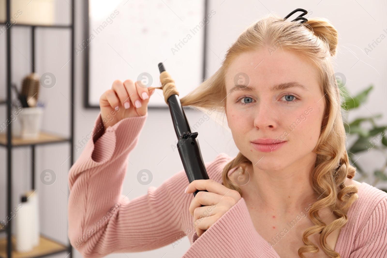 Woman styling her beautiful hair with curling iron indoors Photo of Woman styling her beautiful hair with curling iron indoors