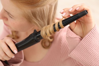 Photo of Woman curling her beautiful hair indoors, closeup