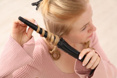 Photo of Woman curling her beautiful hair indoors, closeup