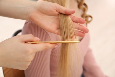 Photo of Hairdresser combing woman's hair in salon, closeup