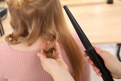 Photo of Hairdresser curling woman's hair in salon, closeup