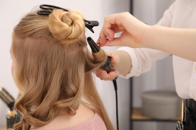 Photo of Hairdresser curling woman's hair in salon, closeup