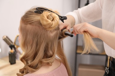 Photo of Hairdresser curling woman's hair in salon, closeup