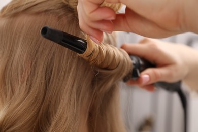 Photo of Hairdresser curling woman's hair in salon, closeup