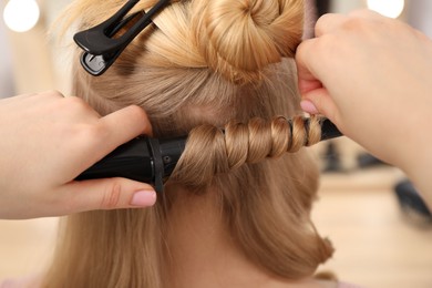 Photo of Hairdresser curling woman's hair in salon, closeup