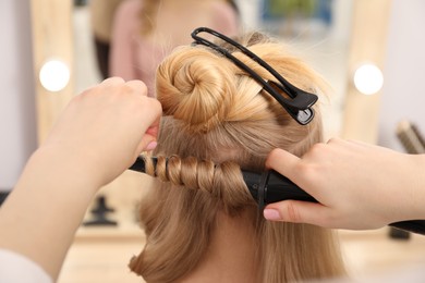 Photo of Hairdresser curling woman's hair in salon, closeup