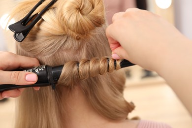 Photo of Hairdresser curling woman's hair in salon, closeup