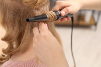 Photo of Hairdresser curling woman's hair in salon, closeup