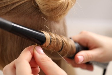 Photo of Hairdresser curling woman's hair in salon, closeup
