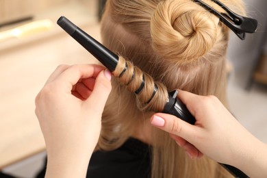 Photo of Hairdresser curling woman's hair in salon, closeup