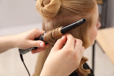 Photo of Hairdresser curling woman's hair in salon, closeup