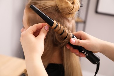 Photo of Hairdresser curling woman's hair in salon, closeup