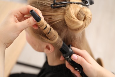Photo of Hairdresser curling woman's hair in salon, closeup