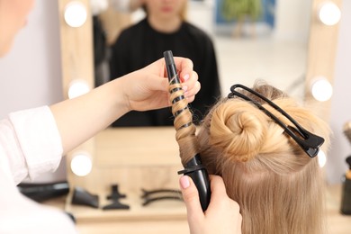 Photo of Hairdresser curling woman's hair in salon, closeup