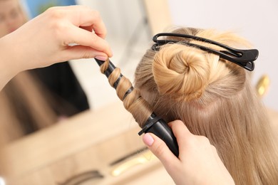 Photo of Hairdresser curling woman's hair in salon, closeup