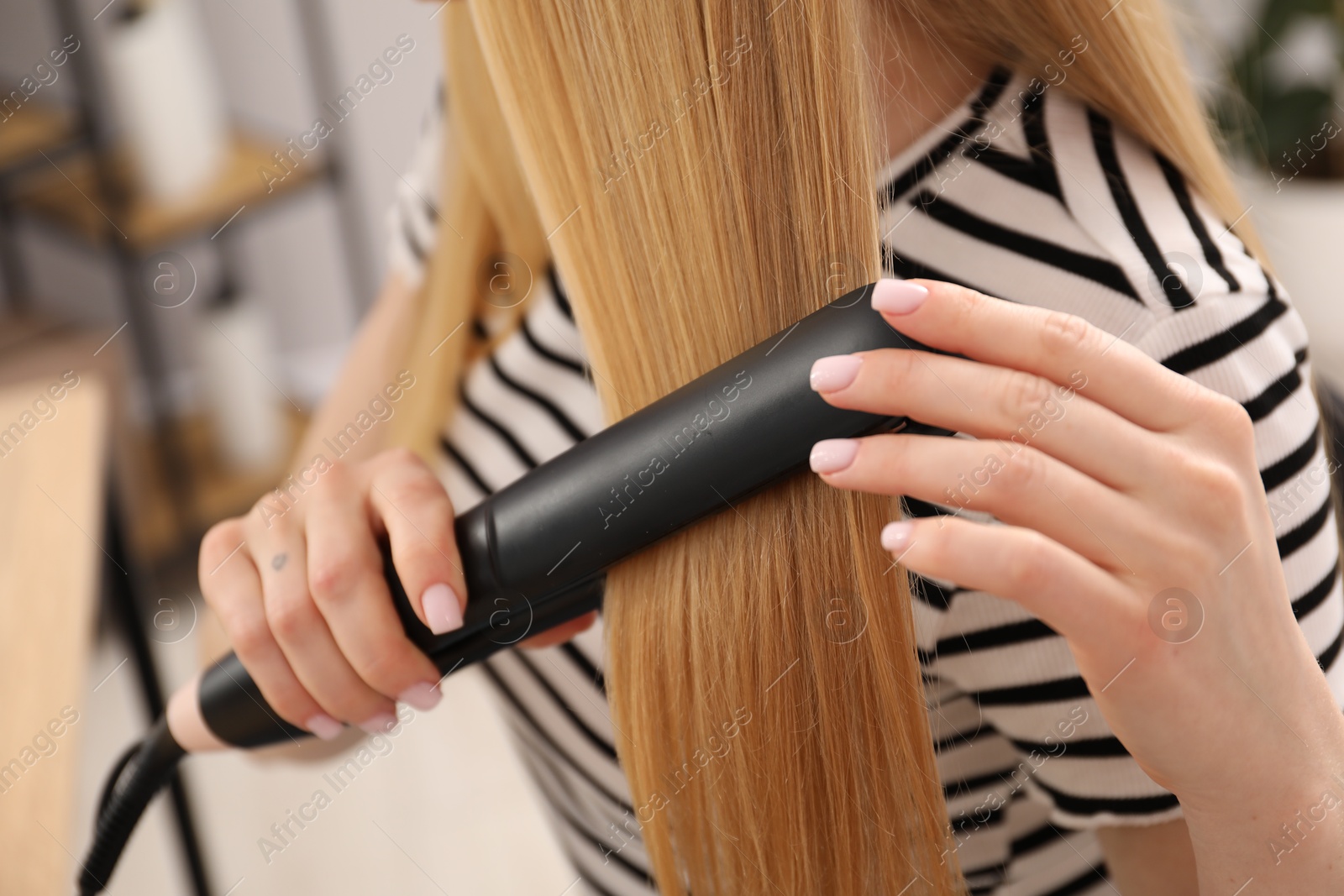Woman straightening her beautiful long hair indoors, closeup Photo of Woman straightening her beautiful long hair indoors, closeup