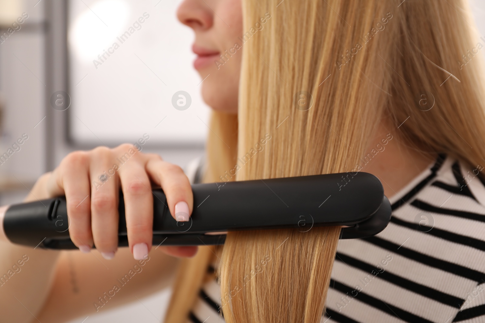 Woman straightening her beautiful long hair indoors, closeup Photo of Woman straightening her beautiful long hair indoors, closeup