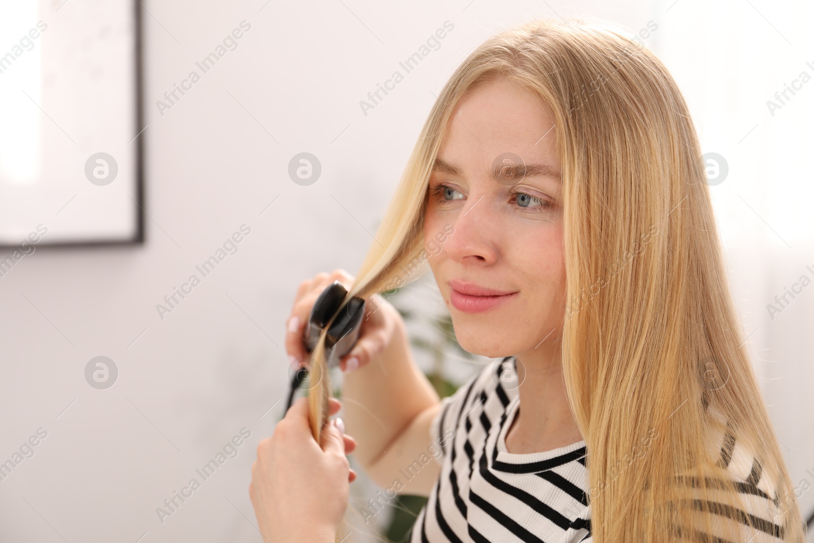 Woman straightening her beautiful long hair indoors. Space for text Photo of Woman straightening her beautiful long hair indoors. Space for text
