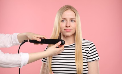 Photo of Hairdresser straightening woman's hair on pink background