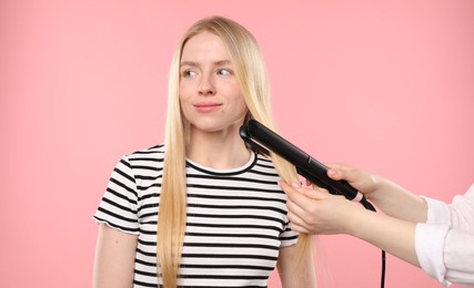 Photo of Hairdresser straightening woman's hair on pink background