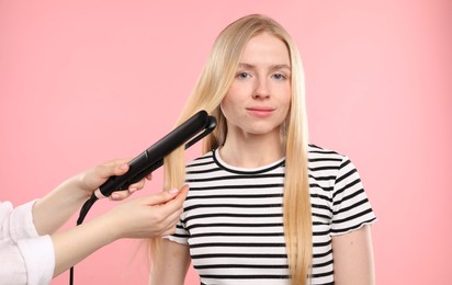 Photo of Hairdresser straightening woman's hair on pink background