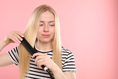 Photo of Woman straightening her hair on pink background. Space for text