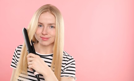 Photo of Woman straightening her hair on pink background. Space for text