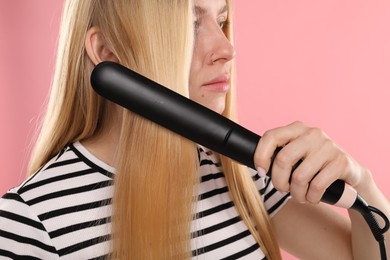 Photo of Woman straightening her beautiful long hair on pink background, closeup