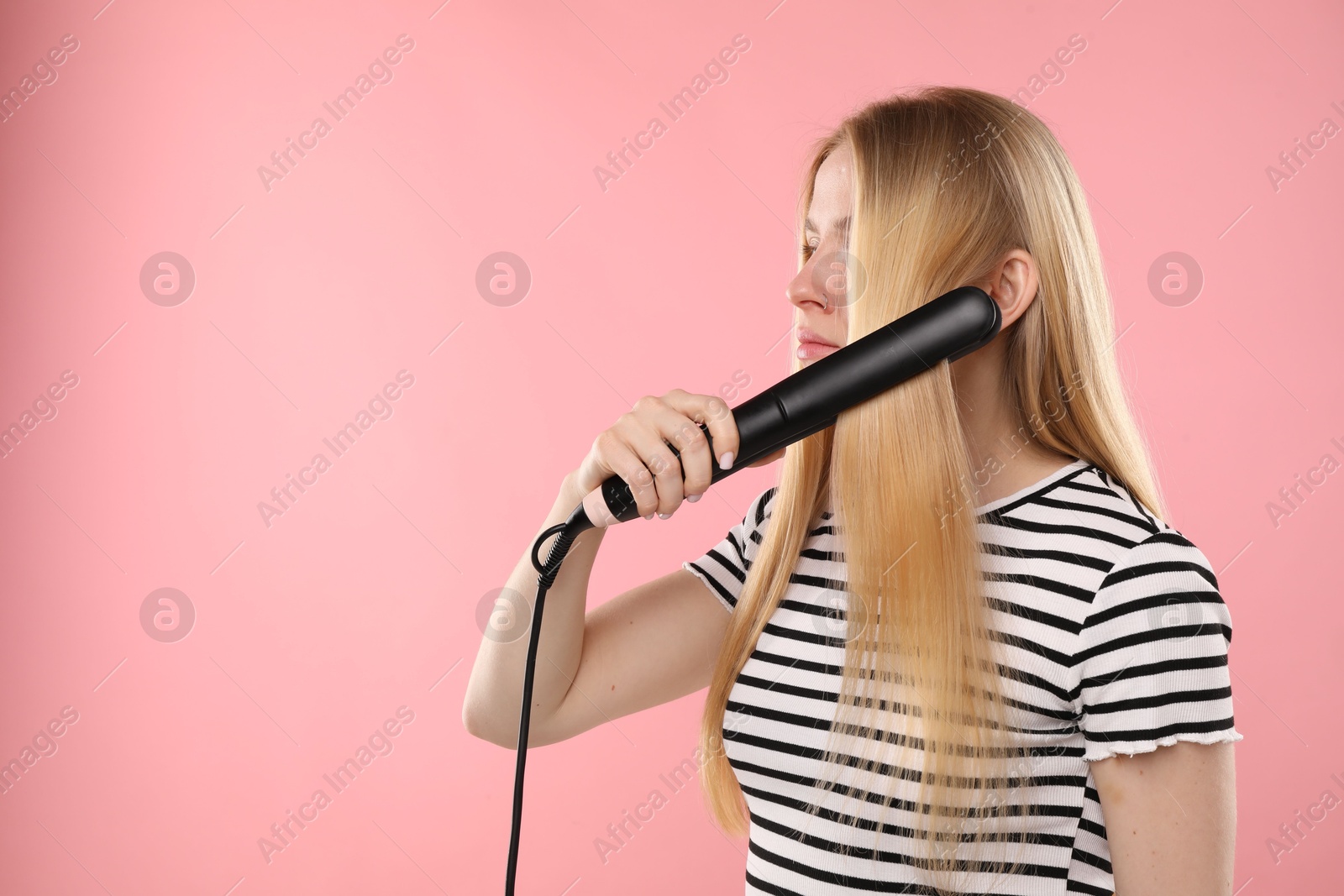 Woman straightening her hair on pink background. Space for text Photo of Woman straightening her hair on pink background. Space for text