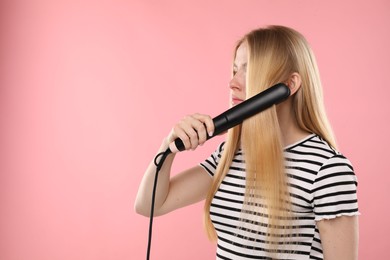 Photo of Woman straightening her hair on pink background. Space for text