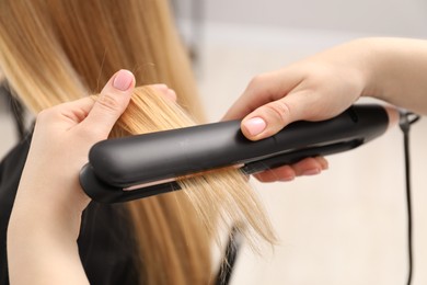 Photo of Hairdresser straightening woman's hair in salon, closeup